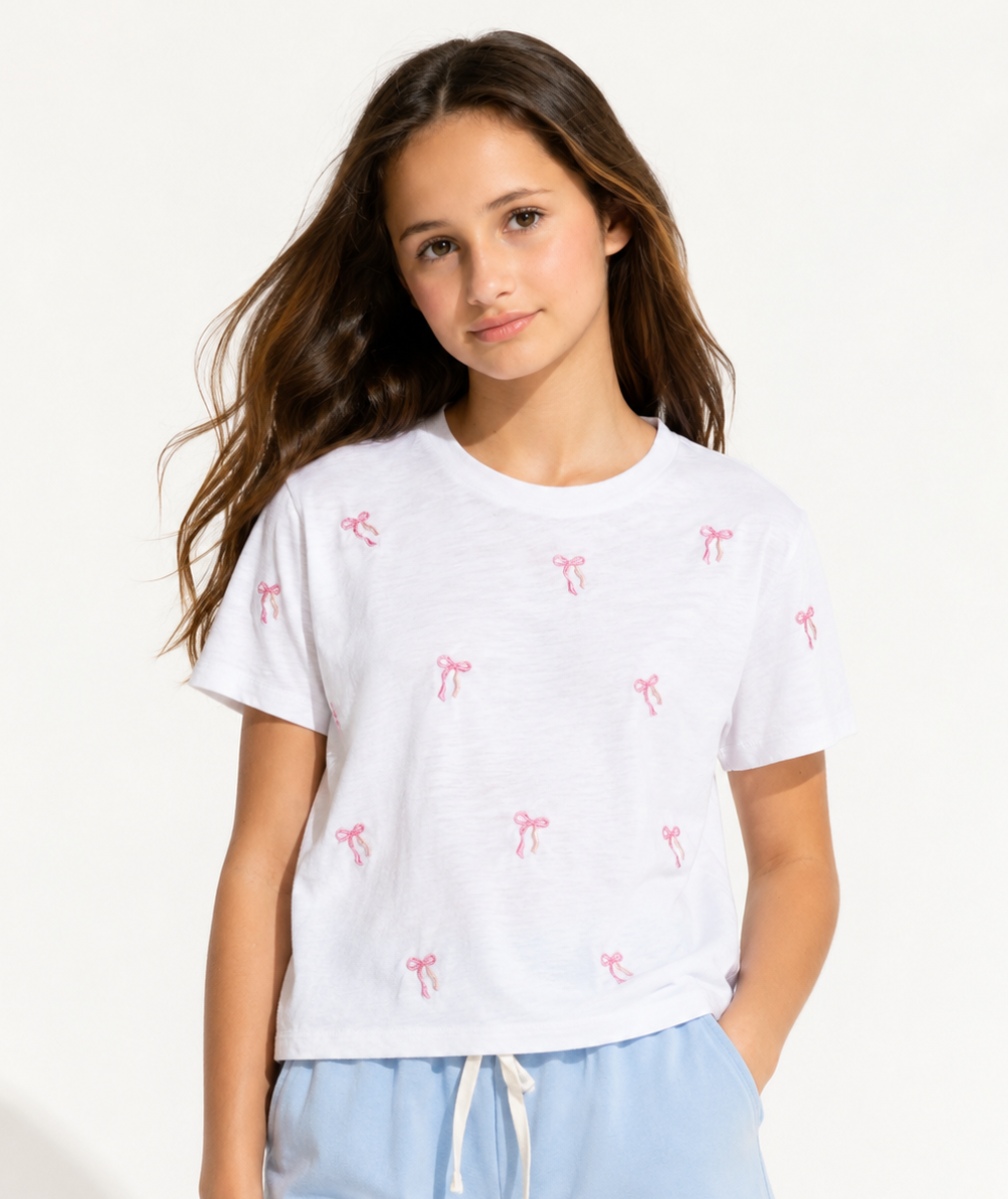 Model wearing the KatieJ NYC Tween Fearless white crop tee with pink embroidered bows, crew neckline, and short sleeves