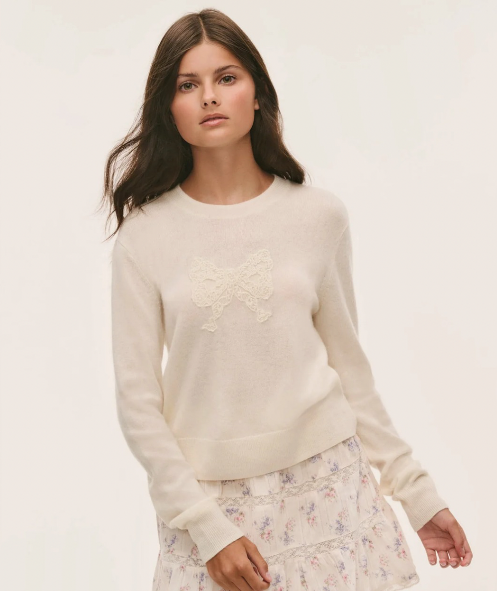 Model wearing the LoveShackFancy Tween Zolee Lace Bow Pullover in Cozy Ivory with tonal lace bow, crew neckline, long sleeves, and ribbed trim.
