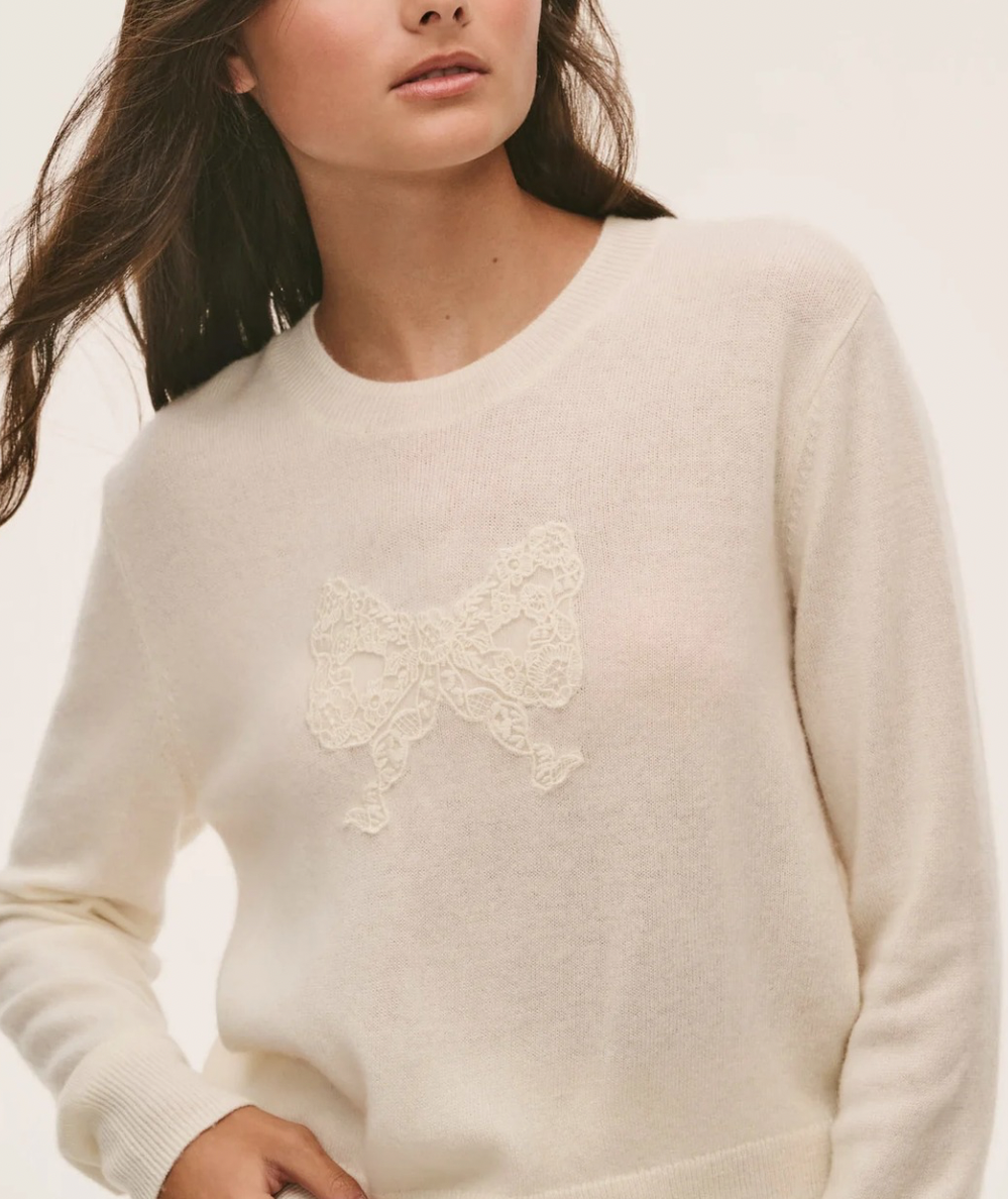Close up of the LoveShackFancy Tween Zolee Lace Bow Pullover in Cozy Ivory with tonal lace bow, crew neckline, long sleeves, and ribbed trim.