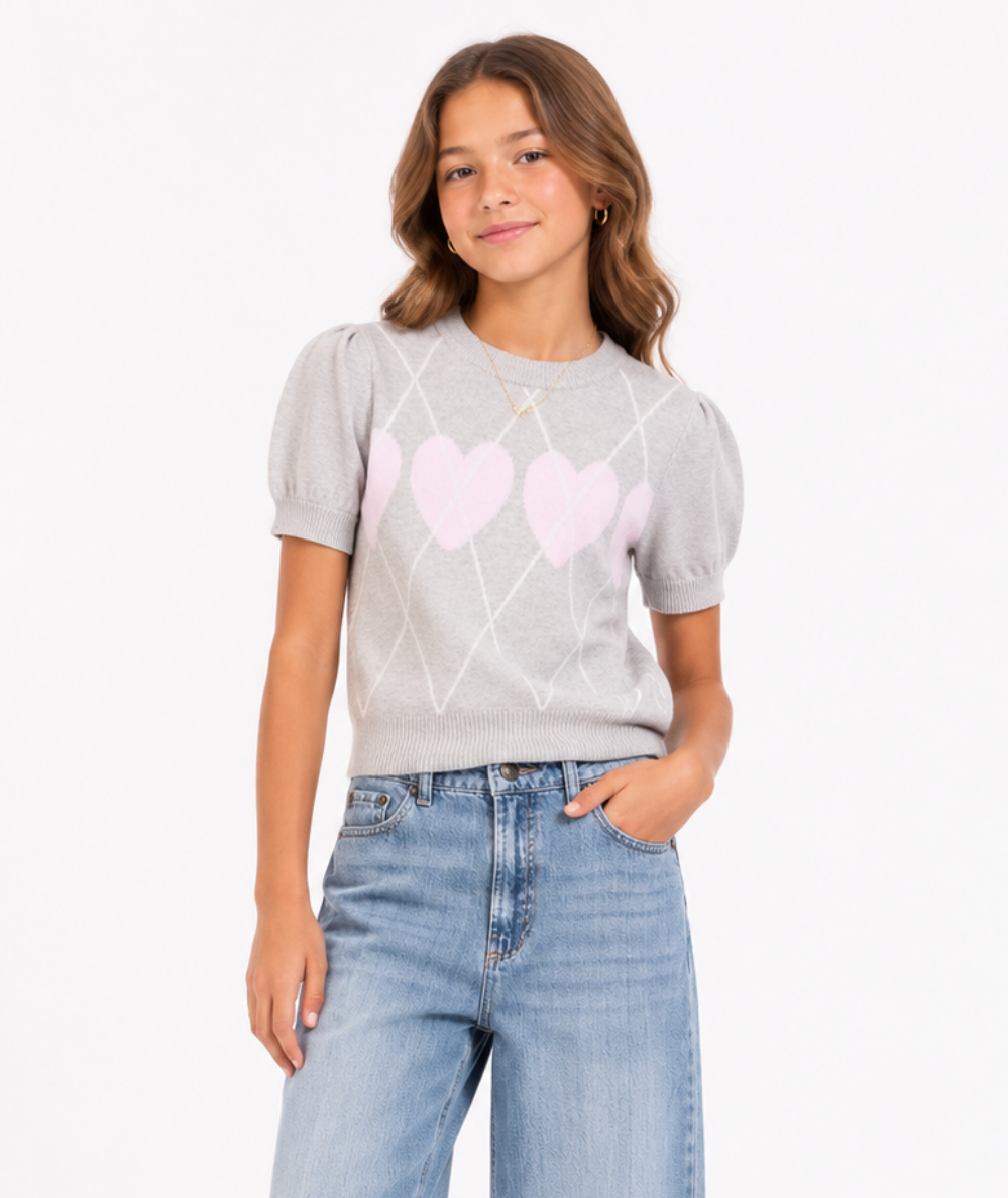 Young model wearing the Design History tween light grey heather short sleeve sweater with pink hearts, white argyle pattern, and puff sleeves.