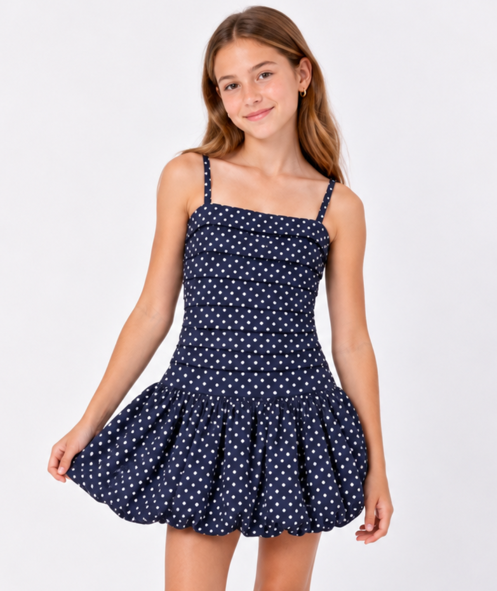 Model wearing the KatieJ NYC Tween Tippy Bubble Dress in evening blue with baby pink polka dots, a pleated bodice, slim straps, and a full bubble hem.