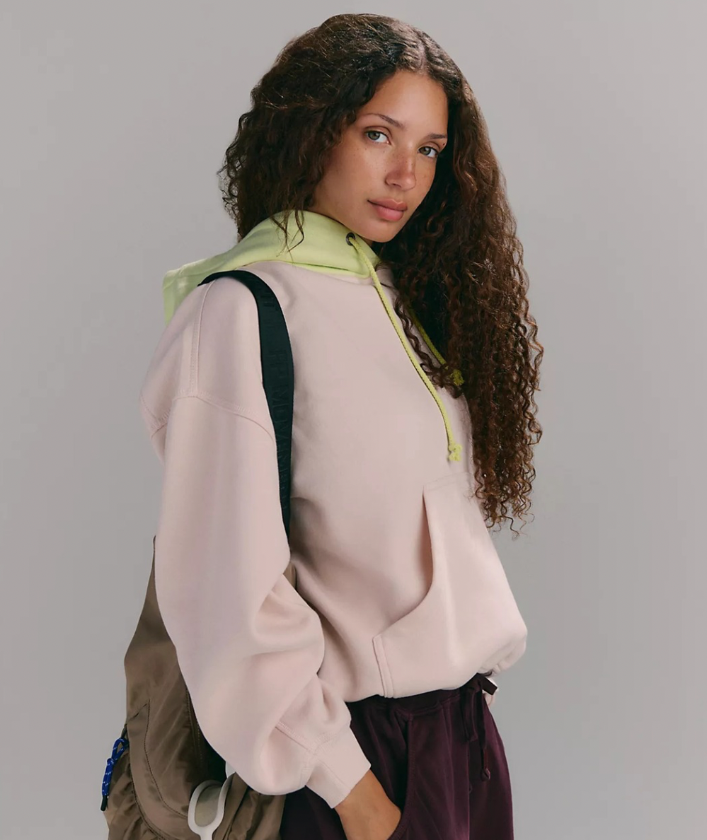 Model wearing the FP Movement Final Call Colorblock Hoodie in Cream Combo with a pale lime drawstring hood and kangaroo pocket.