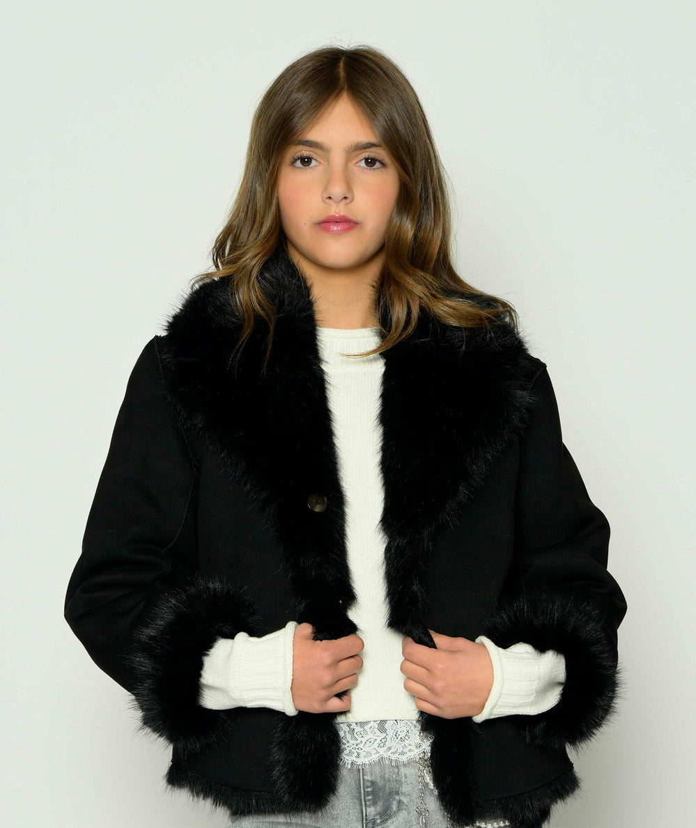 Tween model wearing the black Calvin jacket by KatieJ NYC on its sleek side with faux fur collar and cuffs over a white top - CAKEWISH.