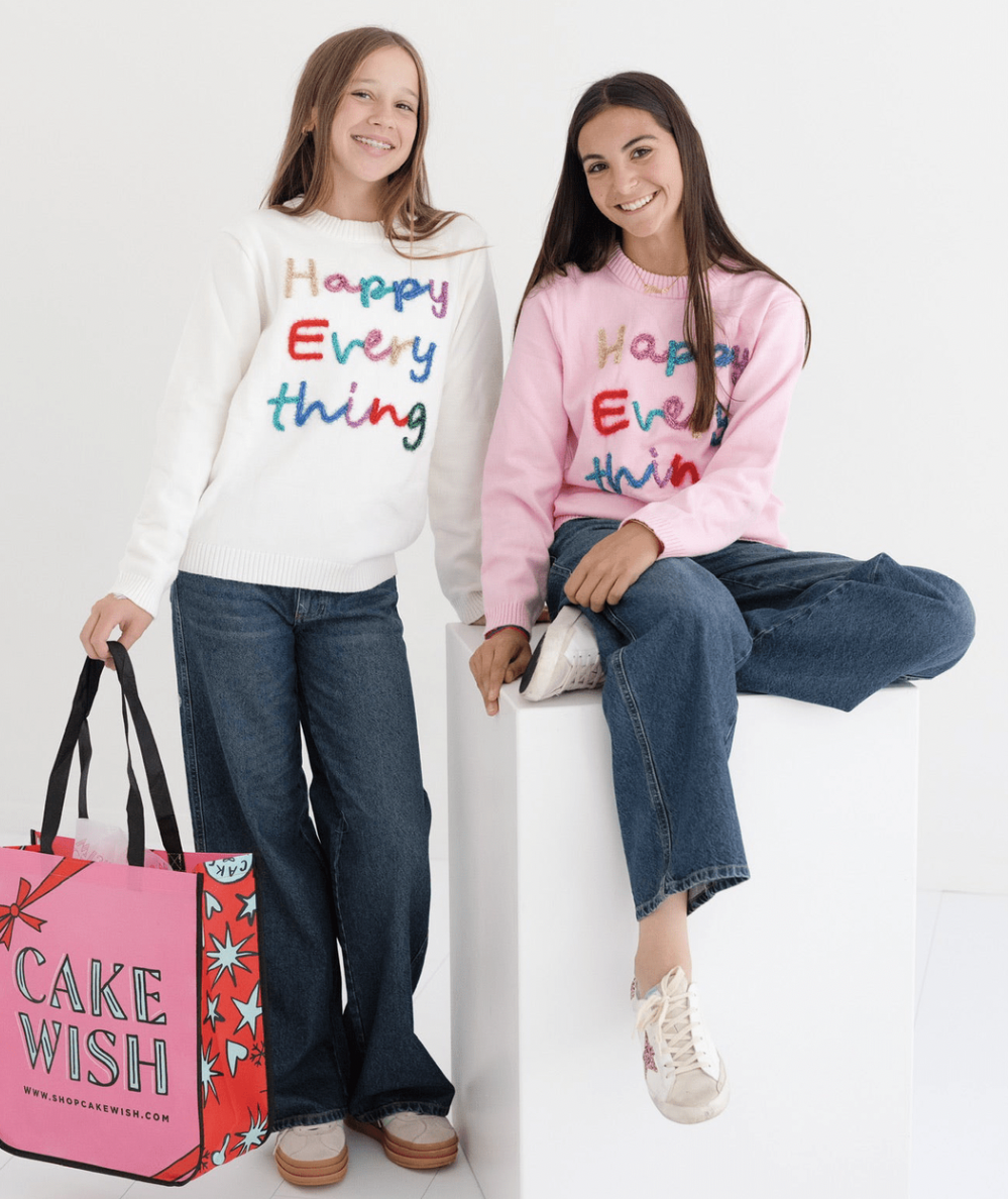 Two tween girls in Happy Everything sweaters with rainbow tinsel lettering and wide-leg jeans by Lola + The Boys - CAKEWISH.