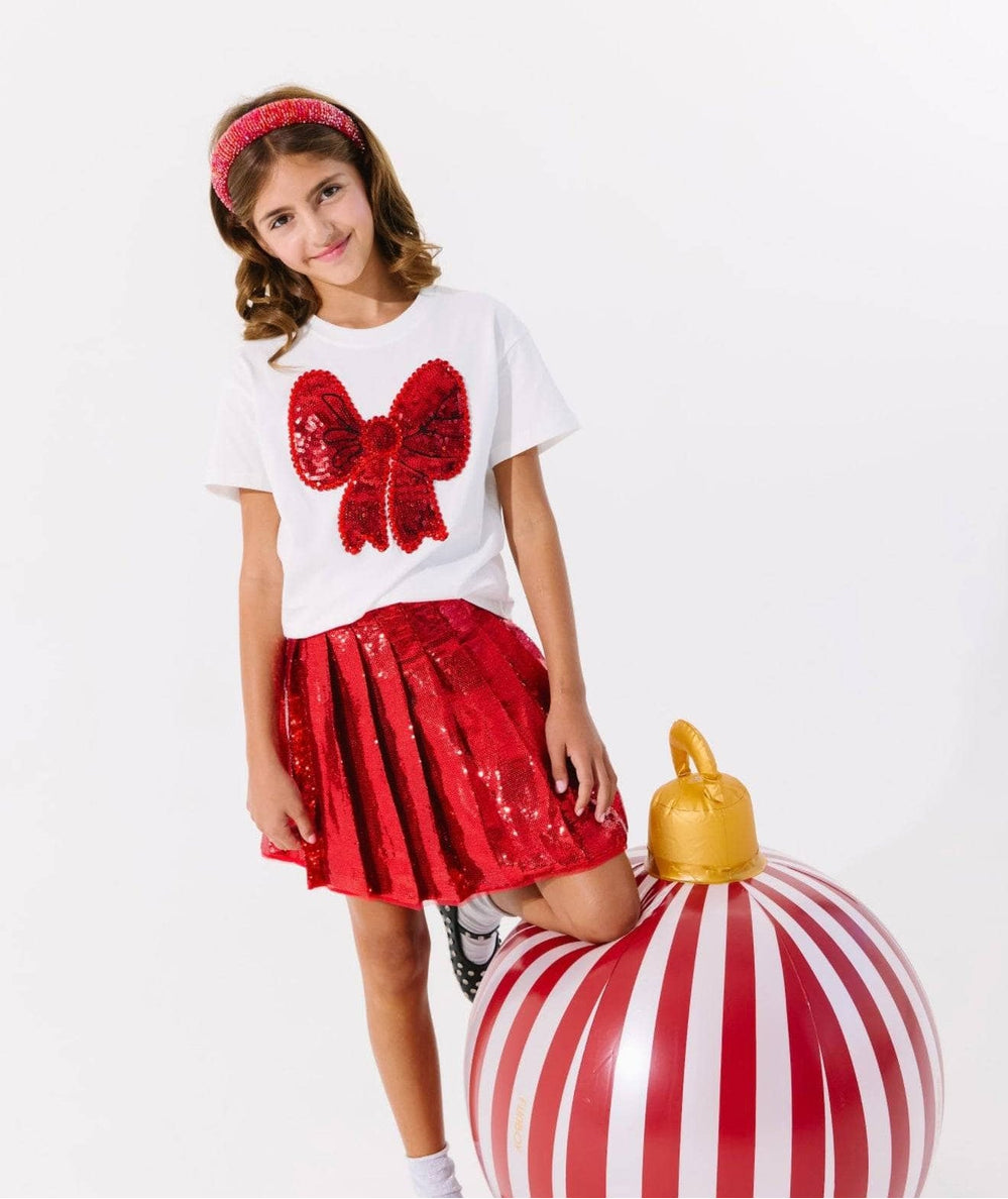 Tween girl wearing the scarlet pleated shimmer skirt with a red bow tee by Lola and the Boys - CAKEWISH.