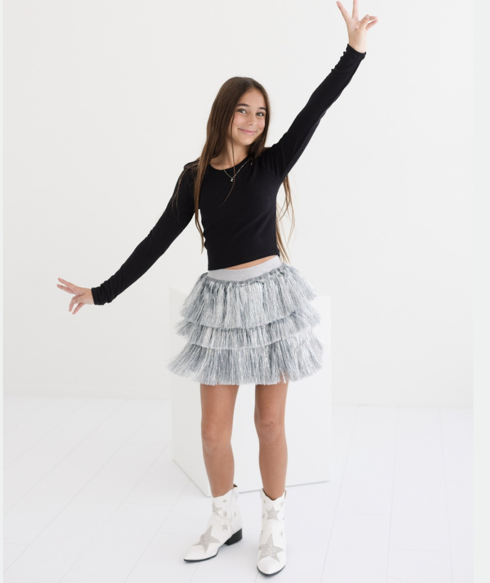 Tween girl in the silver tiered tinsel party skirt with a black long-sleeve top and white star boots by Lola + The Boys - CAKEWISH.