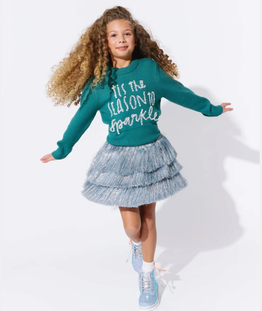 Tween girl jumping in the silver shimmer tinsel skirt with a teal holiday sweater by Lola + The Boys - CAKEWISH.