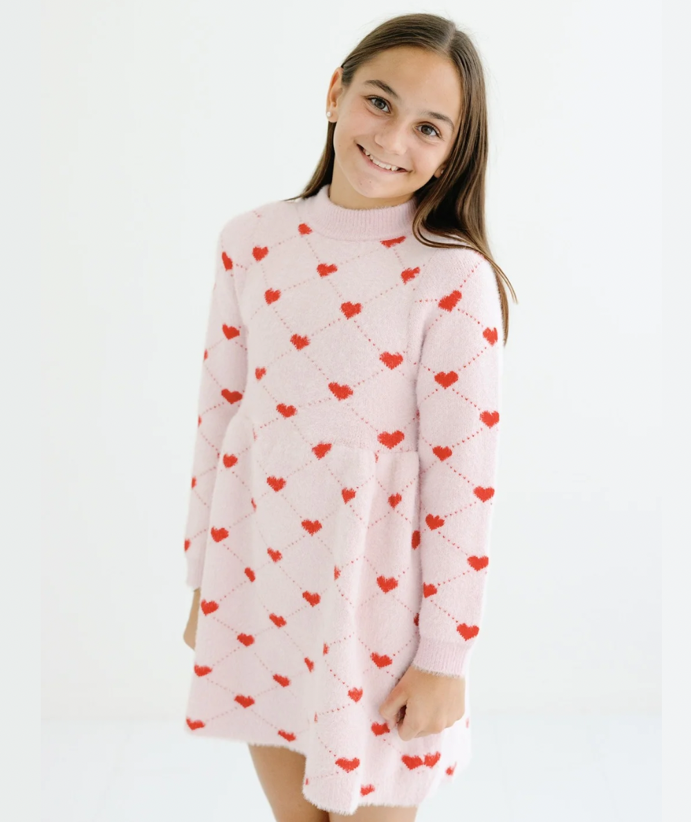 Smiling tween girl in the pink knit Sweetheart Sweater Dress with red hearts by Lola + The Boys - CAKEWISH.