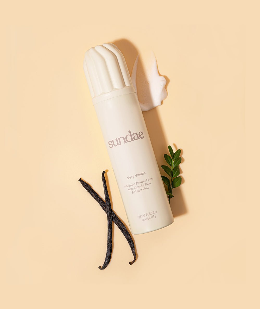 Cream-colored Very Vanilla Whipped Shower Foam can beside vanilla bean pods and a dollop of foam by Sundae Body - CAKEWISH.